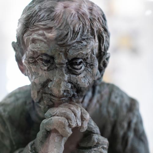 Close up of the sculpture of an old man resting on a walking stick
