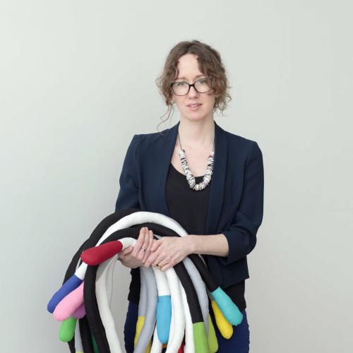 Anna Ray standing in front of a white wall holding tubes of padded fabric.
