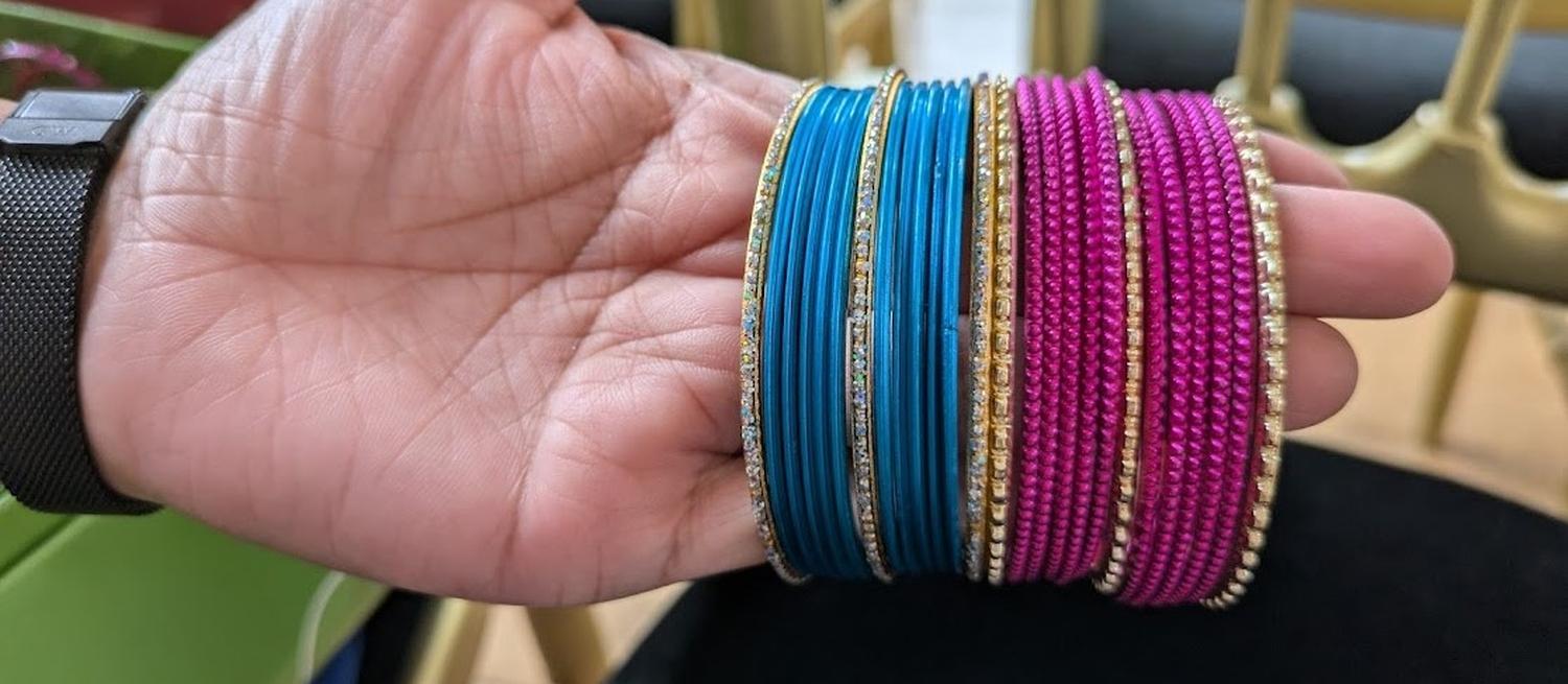 Colour photoraphic image of a hand with a selection of blue and pink metal bangles held on the fingers