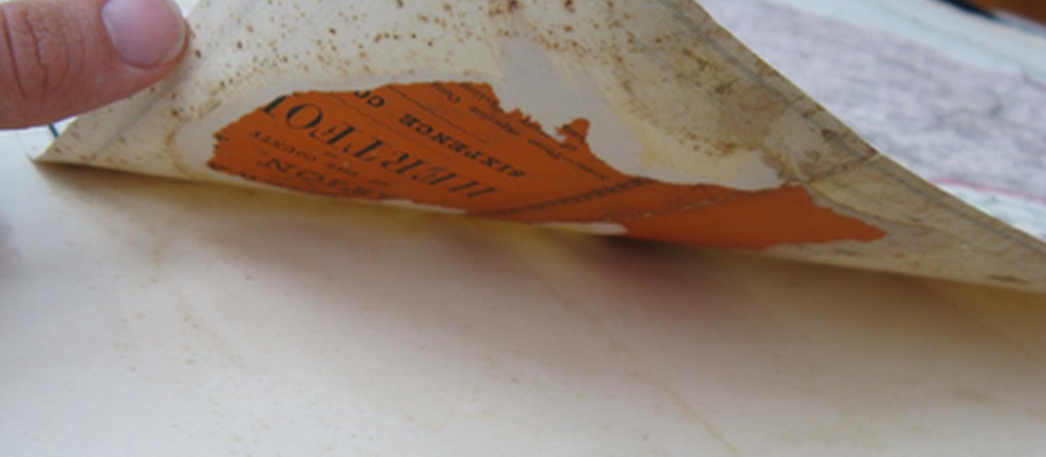 Close-up photograph of a page of an old map being turned by a single finger