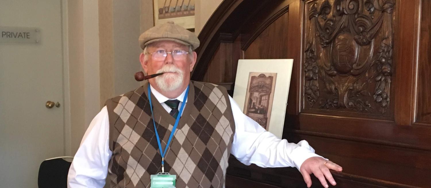 Man dressed in golfing knitted vest and flat cap smoking a pipe