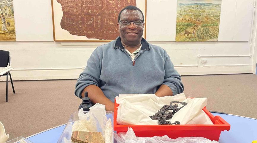 A man sits behind a table with museum artefacts packaged in tissue paper in front of him