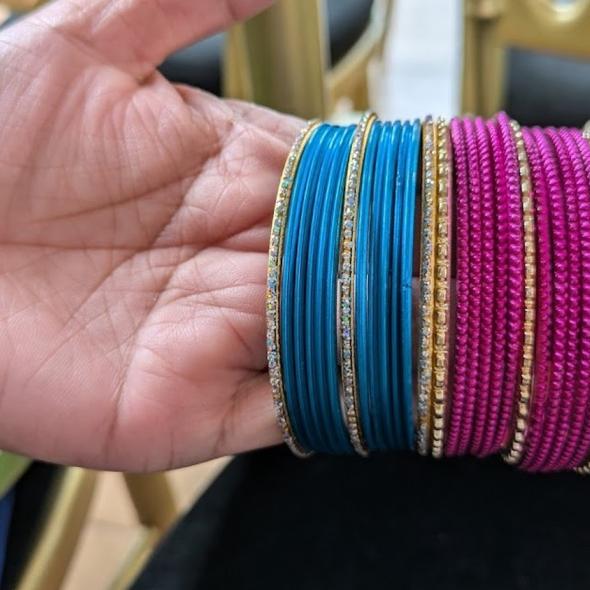 Colour photoraphic image of a hand with a selection of blue and pink metal bangles held on the fingers